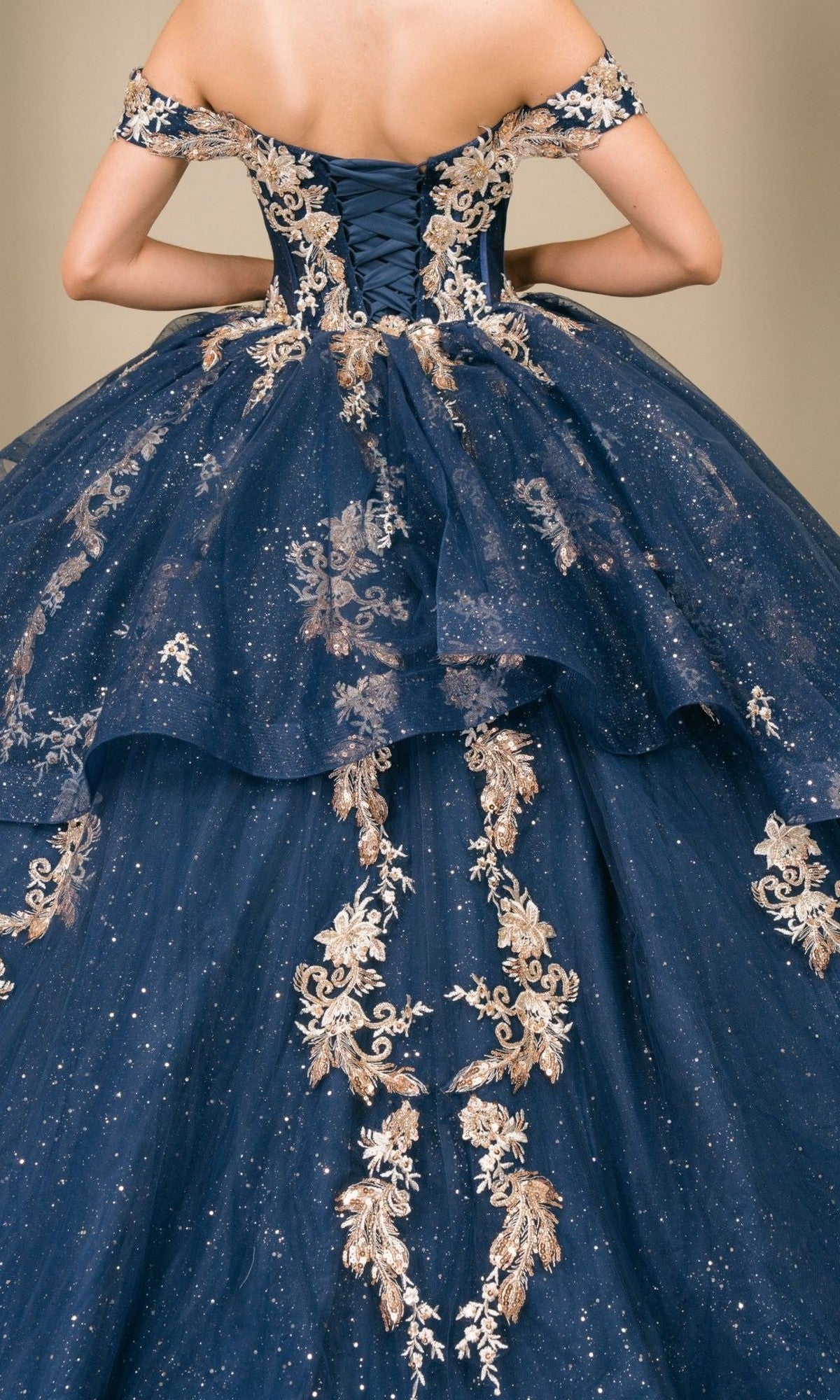 A woman is seen from the back wearing the Quinceanera Dress 8390JQ by Cinderella Couture, an off-shoulder navy ball gown adorned with gold embroidery and glitter.